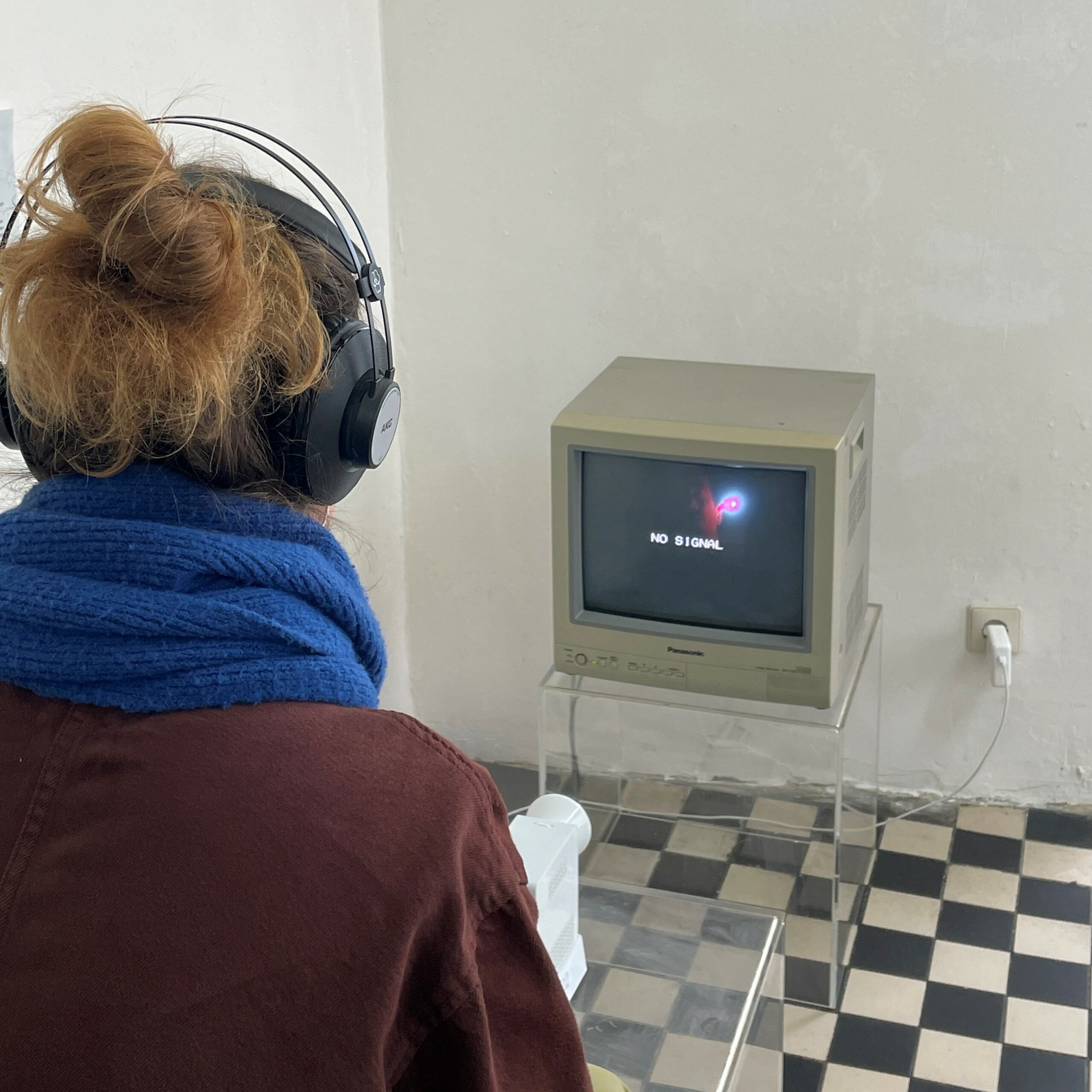 Zu sehen ist eine Kunstinstallation mit einem alten Bildschirm ohne Signal, vor dem eine Frau sitzt.