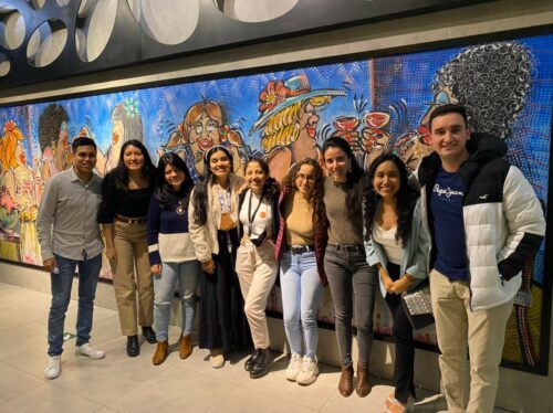 Zu sehen ist eine neunköpfige Alumni-Gruppe vor einer bemalten Wand in Peru