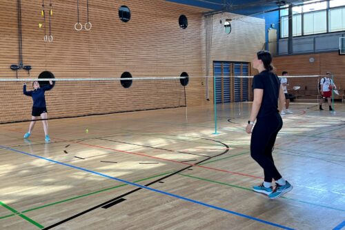 Zu sehen sind zwei Badmintonspielerinnen in der Halle in Action