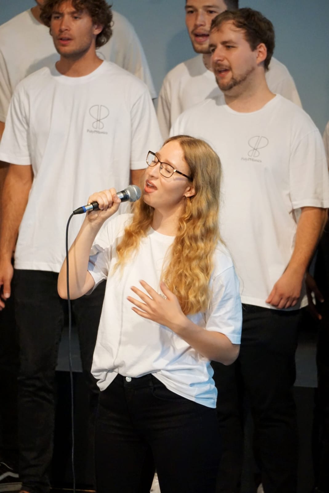 Zu sehen sind mehrere Studierende in weißen T-Shirts singend.