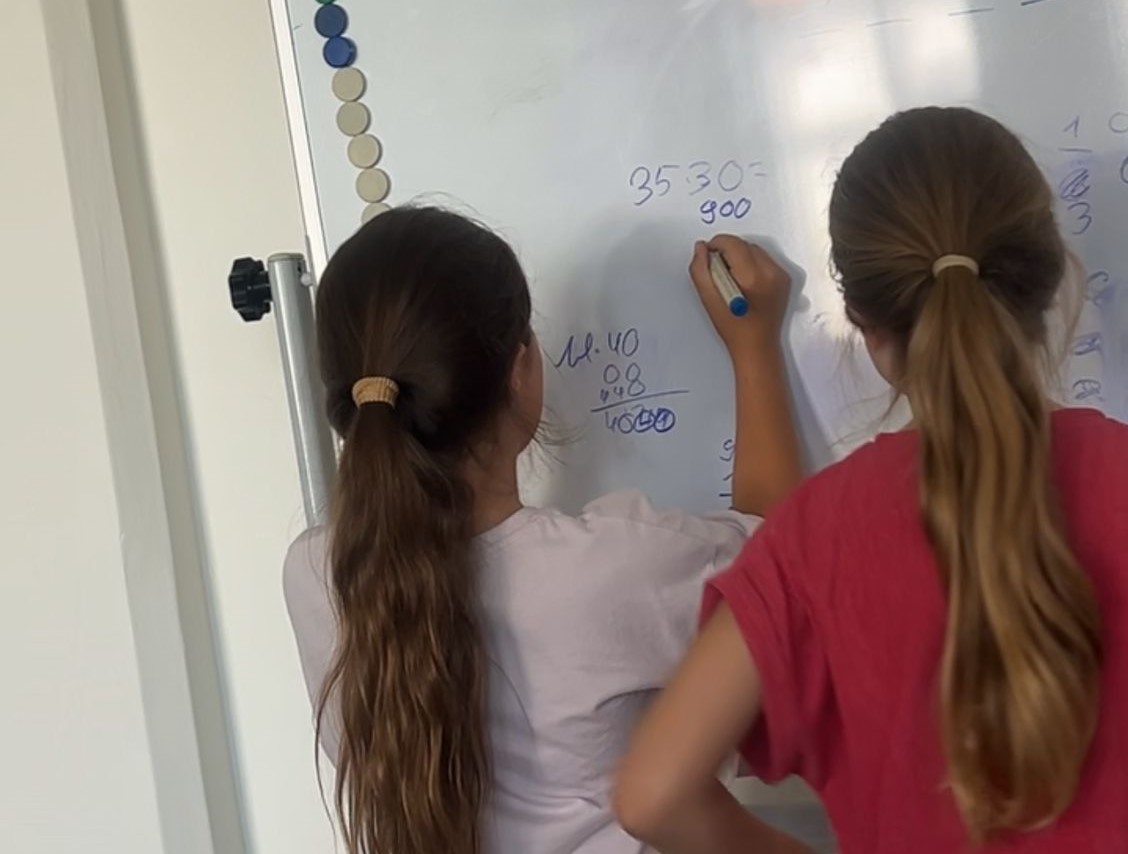 Zu sehen sind zwei Kinder mit dem Rücken zur Kamera, die an einem Whiteboard arbeiten.