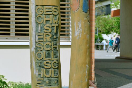 Zu sehen ist ein Baumstamm, in den das Signet Geschwister Scholl Schule geschnitzt ist