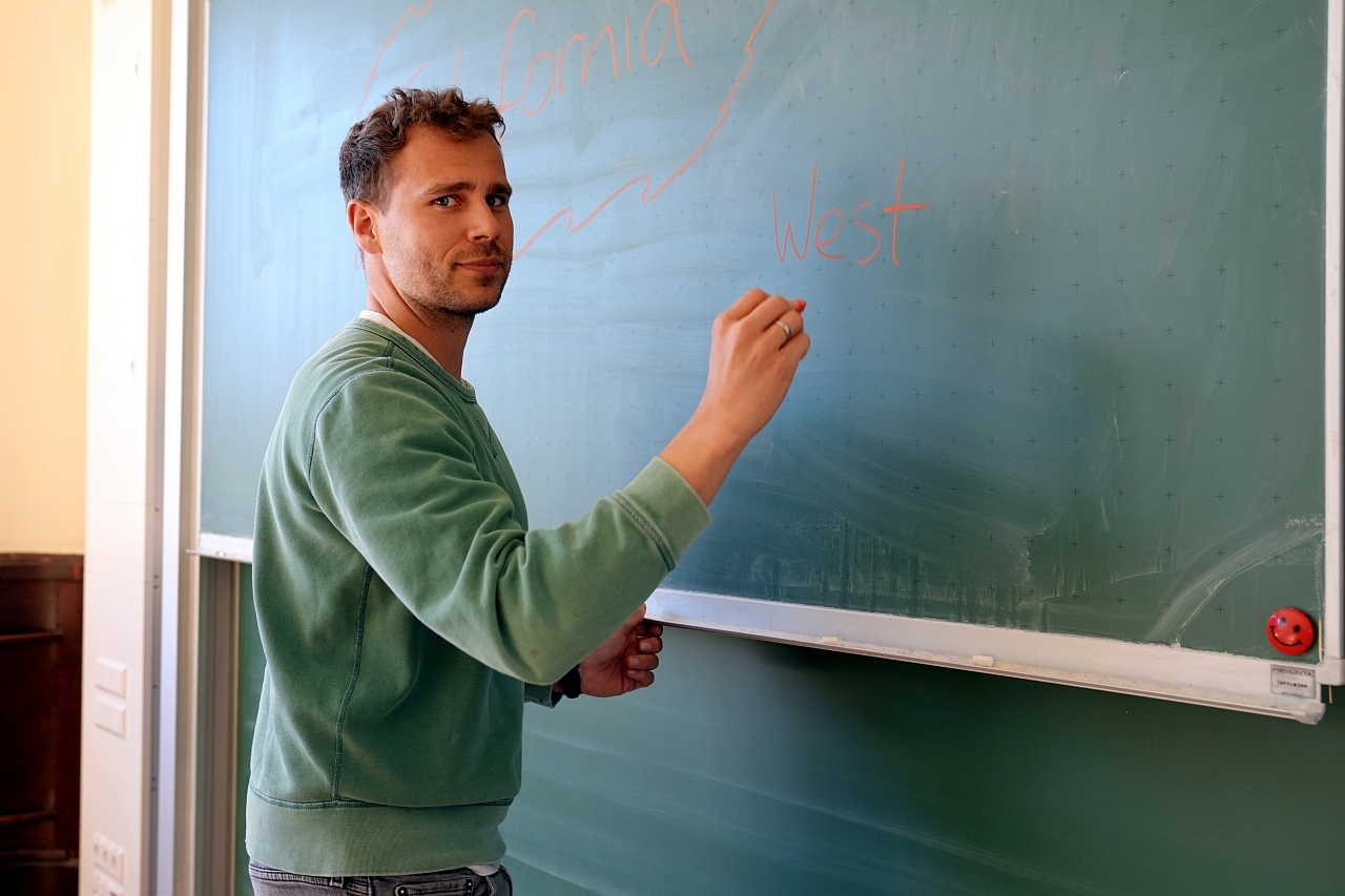 Zu sehen ist ein Lehrer an einer Tafel
